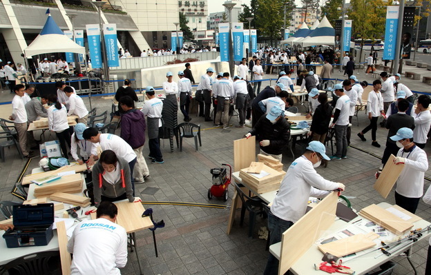 Executives and employees, including Doosan Group CEO Yongmaan Park, crafted handmade furniture at the plaza in front of Doosan Tower in Seoul, to be donated to low-income households.