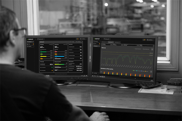 Manager in office overlooking factory and computer screens showing UgoPilot fleet management software dashboard and reporting